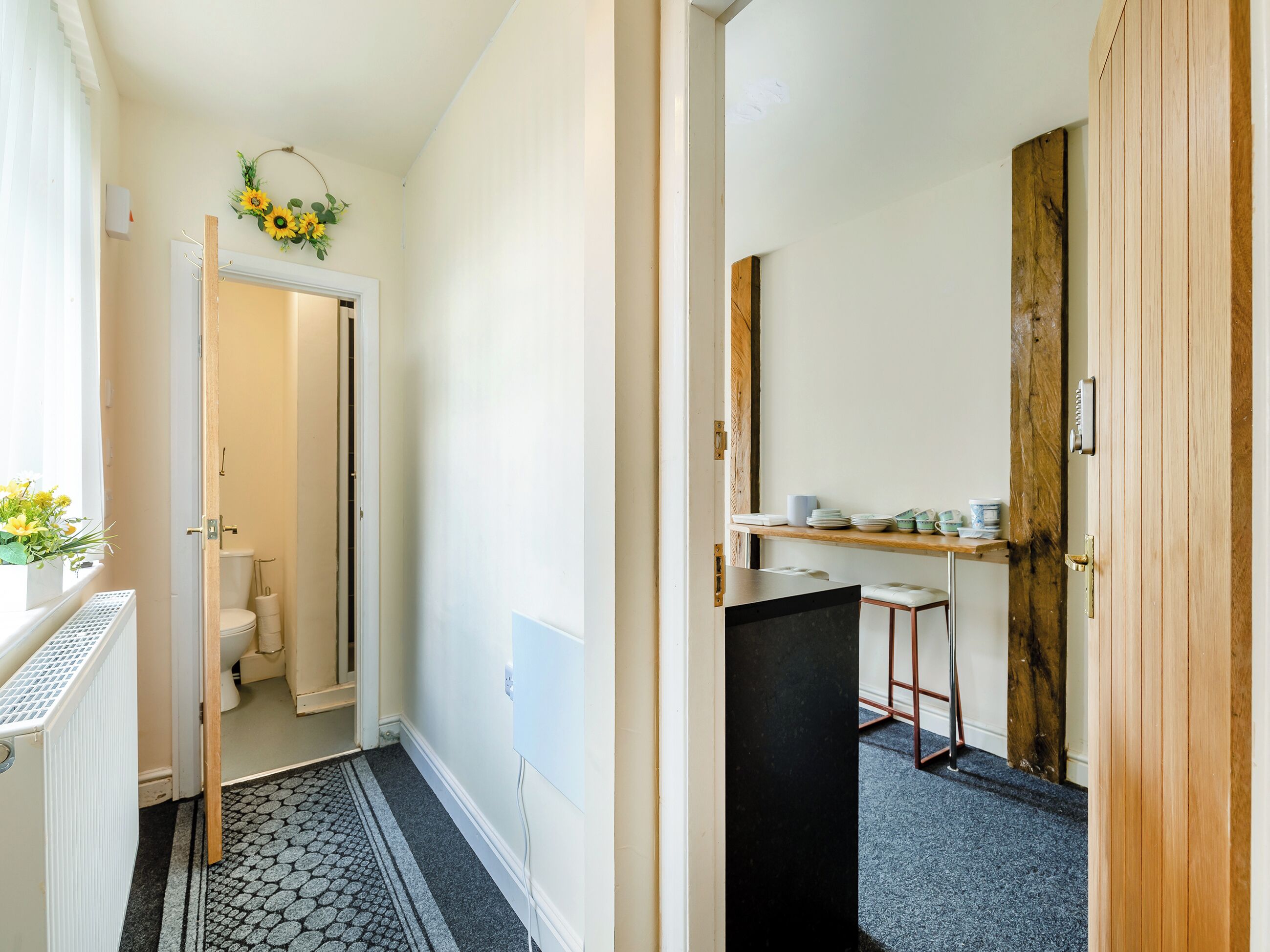 A hallway with a toilet, a radiator, a wooden door, and a shelf with dishes.