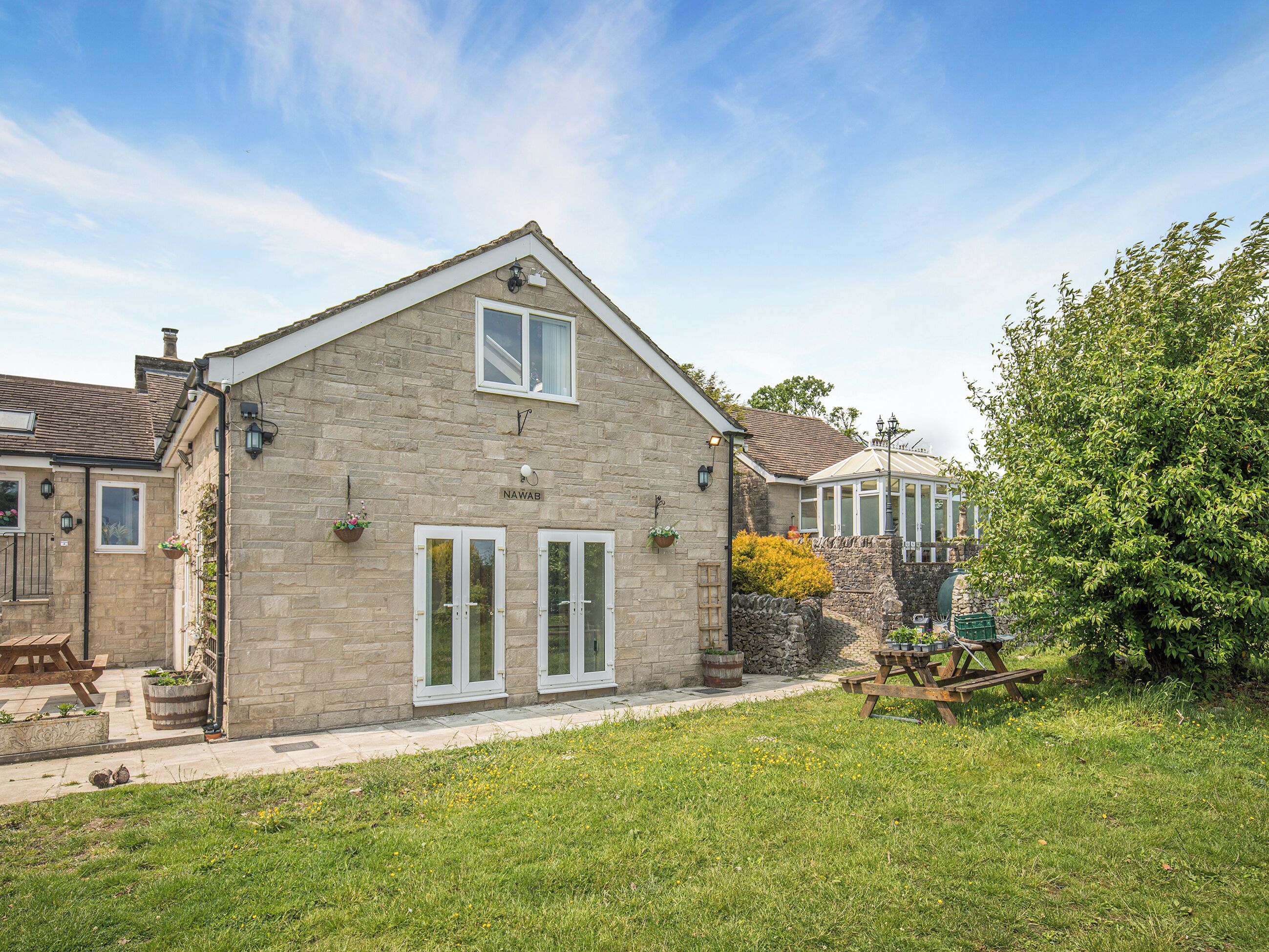 A stone house with a gabled roof, a conservatory, and a well-maintained lawn.