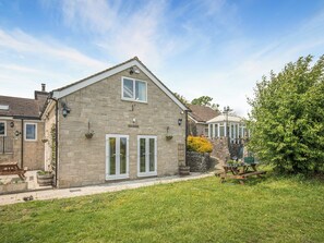 A stone house with a gabled roof, a conservatory, and a well-maintained lawn.
