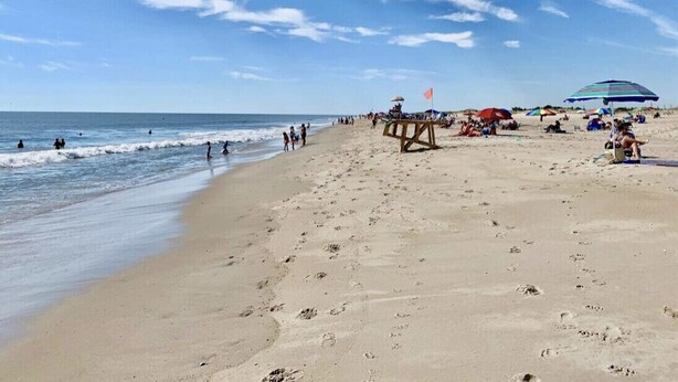 Ein Strand mit Fußspuren, Sonnenschirmen und Menschen.