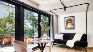 A modern living room with a black sofa, a round table, and a pink chair. There are potted plants outside the large windows. - UTOPIC Campos Elíseos by ULIV (Mexico City)
