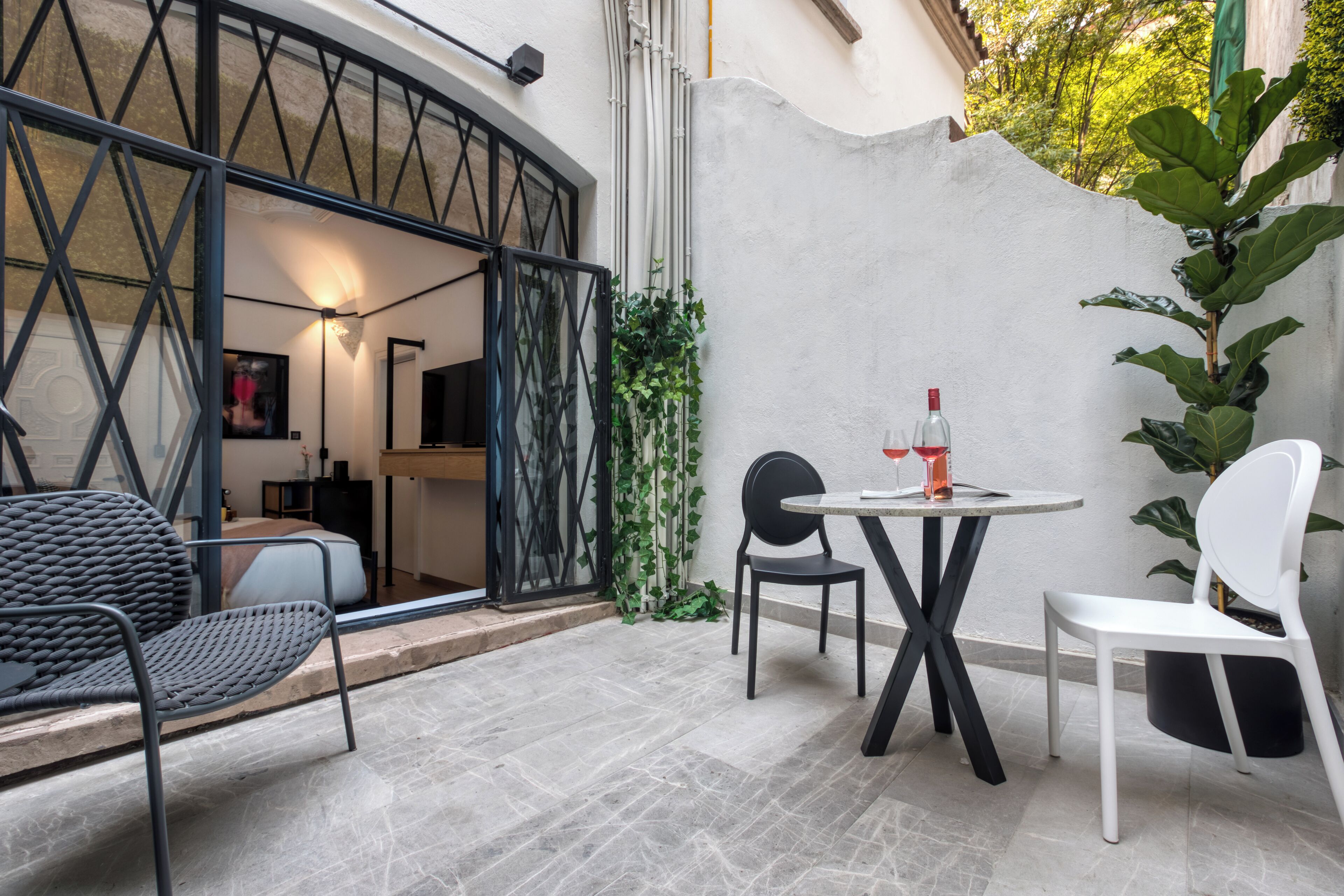 Ein Patio mit rundem Tisch, zwei Stühlen, einer Couch und einem schwarzen Metallgitter.