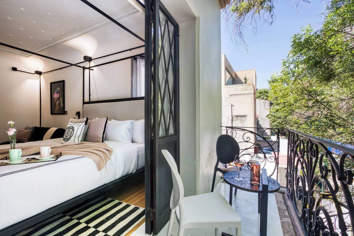 Una camera da letto con un letto, comodino e un balcone con tavolo e sedia.