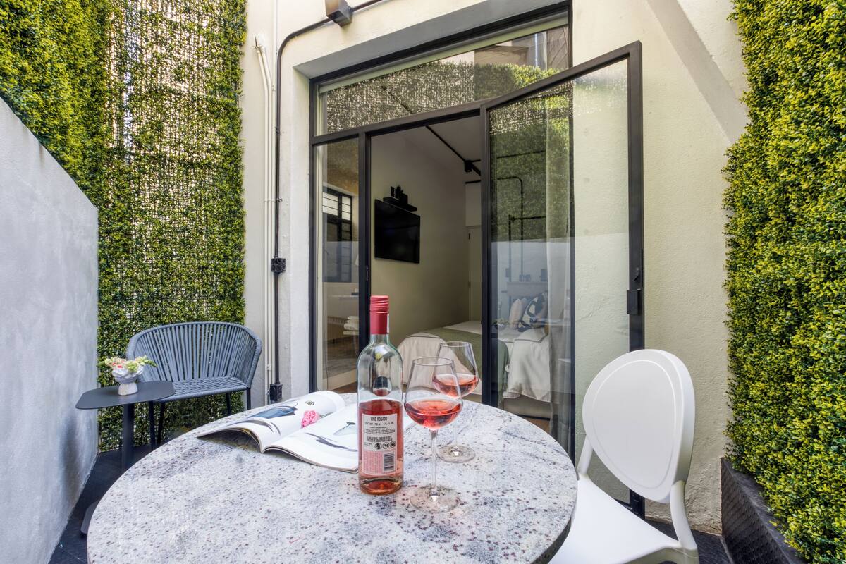 Un piccolo patio con tavolo, sedie e una bottiglia di vino.