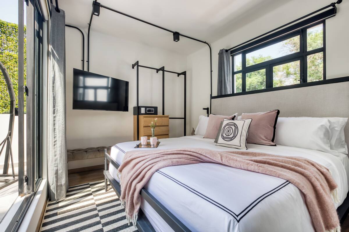 Una camera da letto moderna con un grande letto, una TV a parete e una finestra con vista sul verde.
