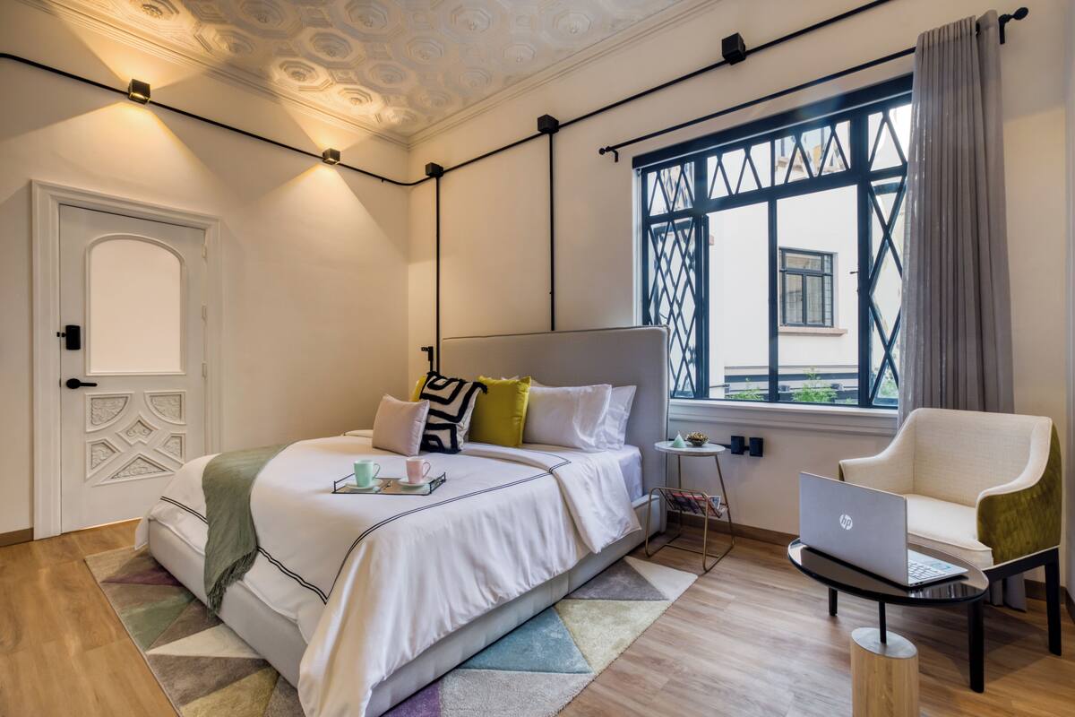 Camera da letto moderna con un letto, un laptop su un comodino e una finestra con vista sull'esterno.