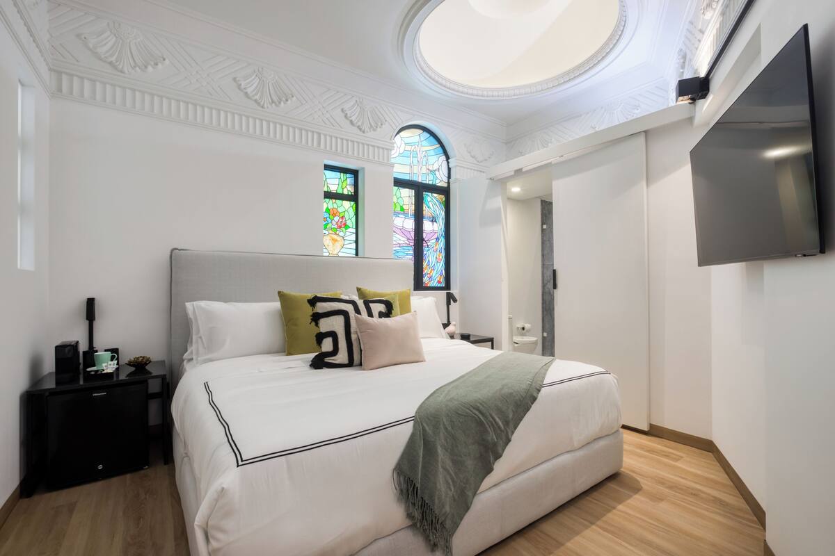 Una camera d'albergo moderna con un letto grande, una televisione a schermo piatto, un comodino e un tavolino con una tazza e un libro.
