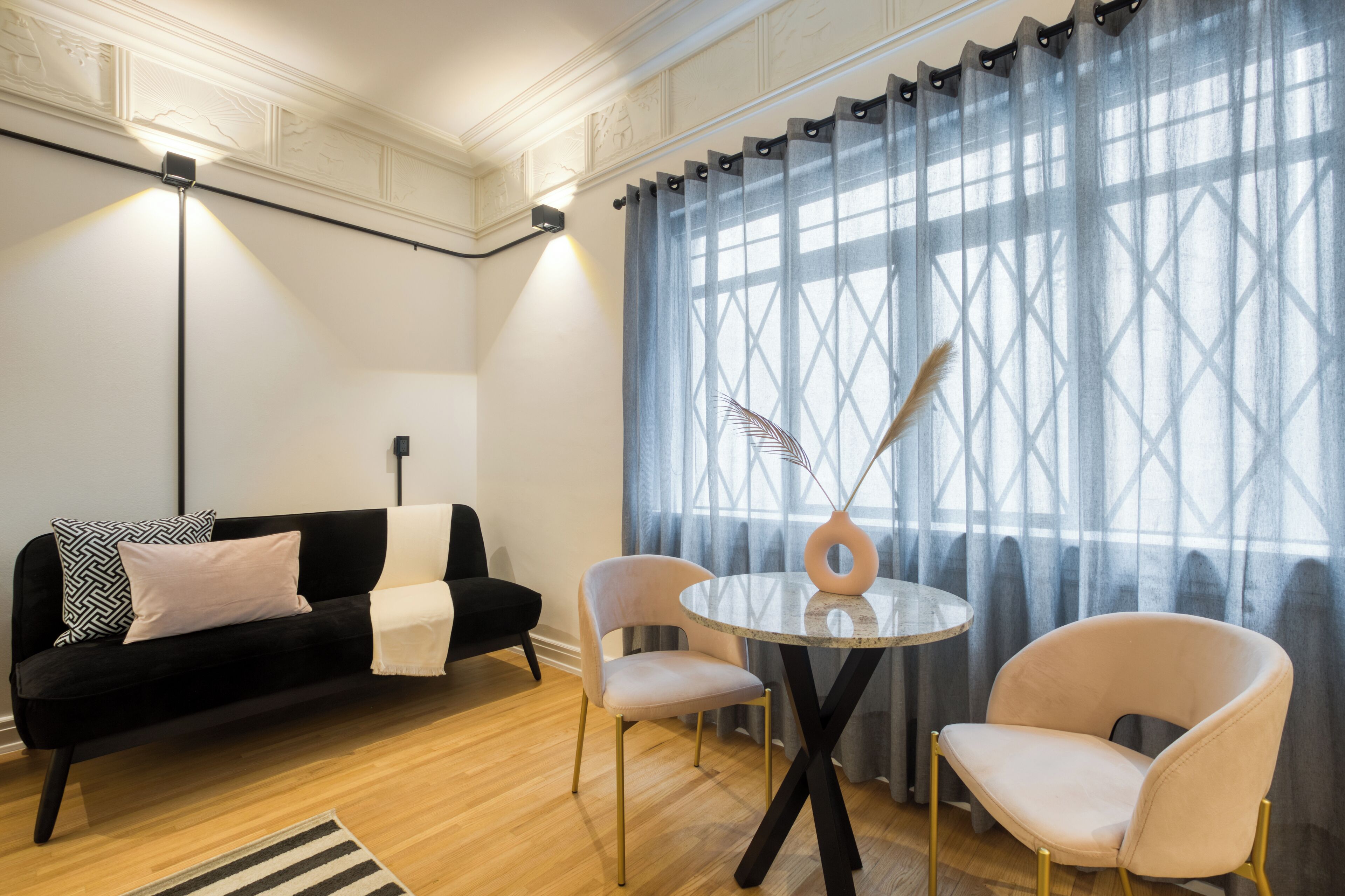 Ein modernes Wohnzimmer mit einer schwarzen Couch, zwei Sesseln, einem runden Tisch und einem großen Fenster mit Vorhängen.