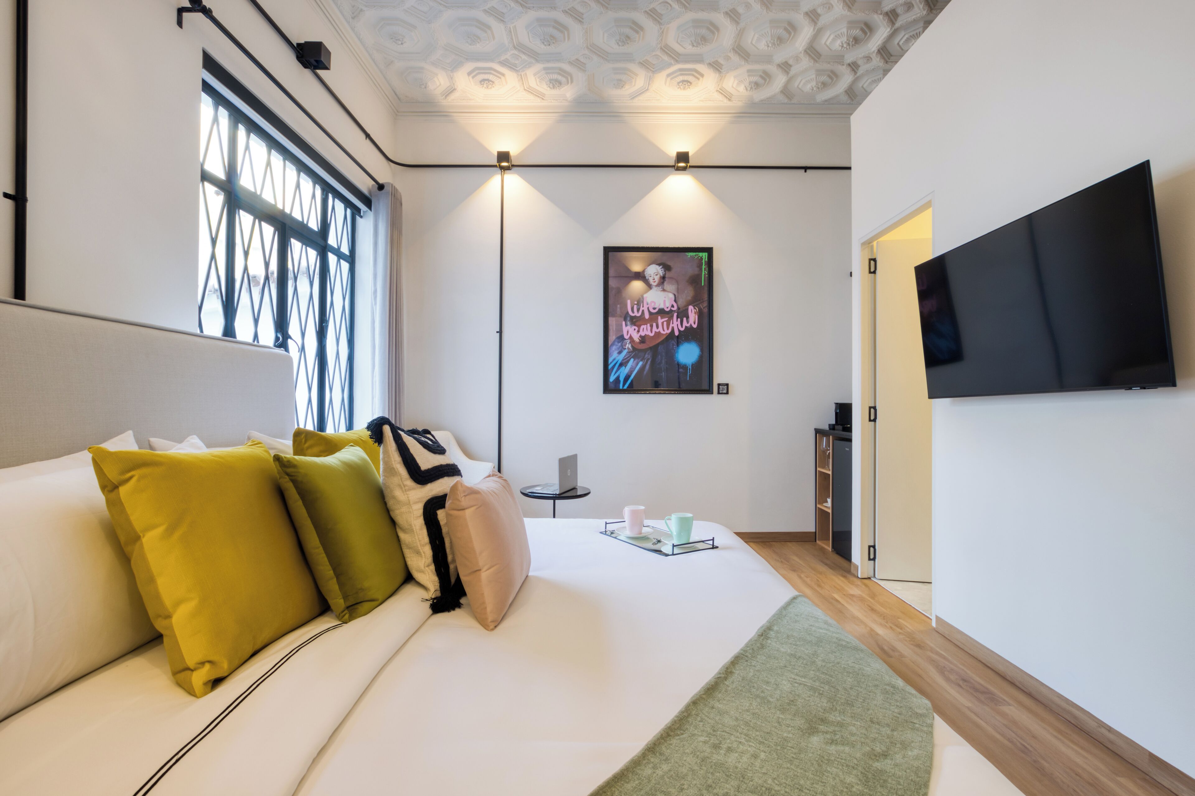 A modern hotel room with a large bed, a flat-screen TV, a window with a view, and a small side table.
