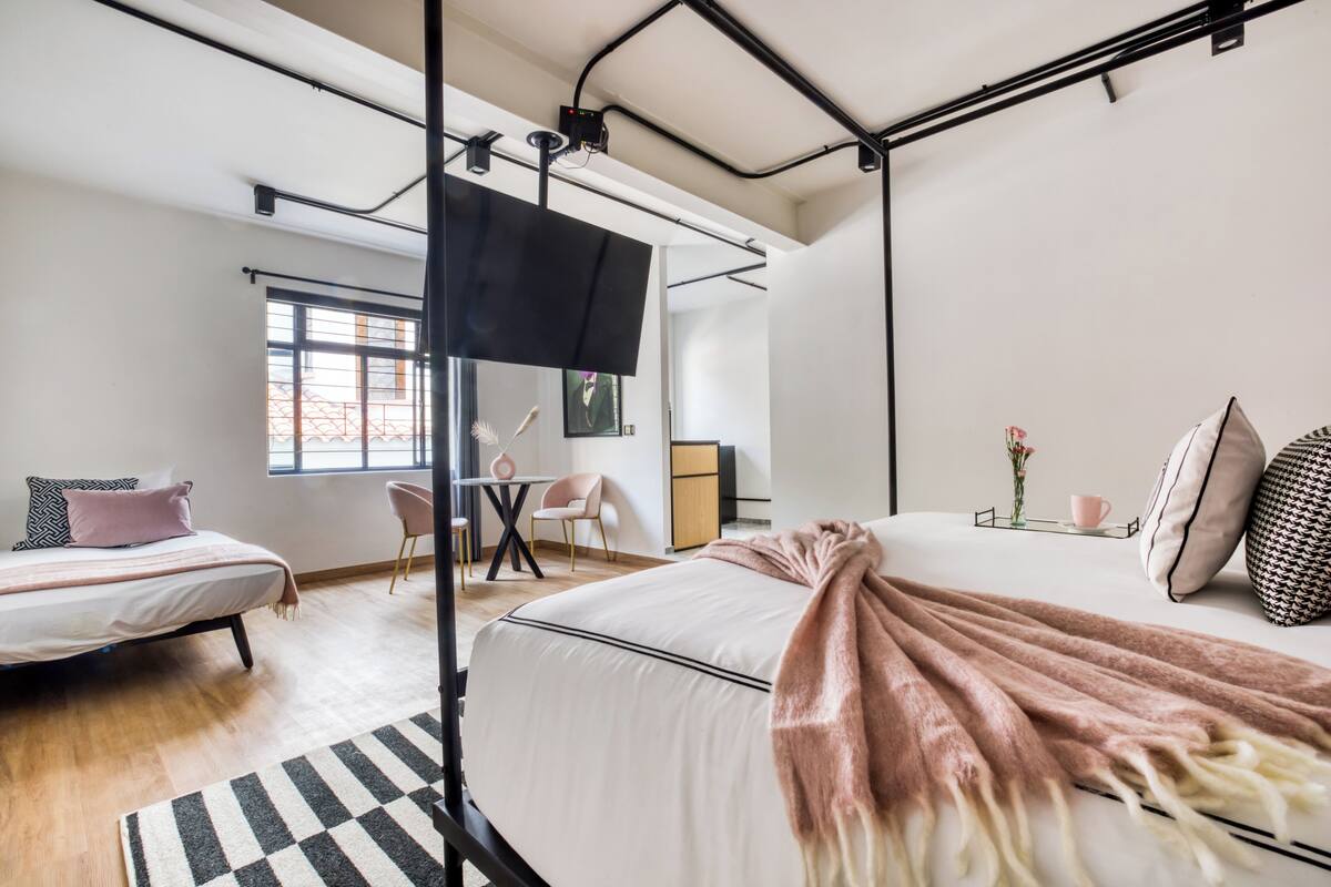 Una camera da letto moderna con un letto grande, un letto più piccolo, una scrivania e una TV a parete.