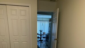 A bedroom with a patterned bedspread, a closed door, and a view into a dining area.