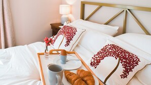 A neatly made bed with white linens and decorative pillows, a bedside table with a lamp, and a tray with croissants, a mug, and a small vase with flowers. - 1 bedroom accommodation in Great Bealings (Great Bealings)
