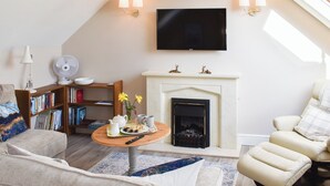 A cozy living room with a fireplace, a flat-screen TV, a bookshelf, and a comfortable seating area. - 1 bedroom accommodation in Great Bealings (Great Bealings)