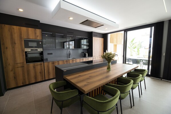 A modern kitchen with a wooden island, green chairs, and a large window.