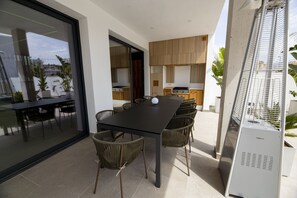 A modern outdoor dining area with a black table and wicker chairs, a glass door leading to a balcony, and a metal grill on the right. - A magnificent contemporary villa right in the city center, a 3-minute walk from the beach and restaurants. (Empuriabrava)
