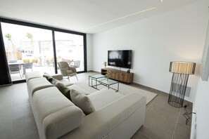 A modern living room with a large sofa, a coffee table, and a TV mounted on the wall.