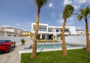 A modern house with a swimming pool, palm trees, and a red sports car parked in front.