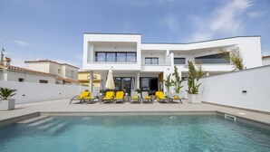 Un área de piscina moderna con una piscina cristalina, sillas de descanso amarillas y un edificio blanco de varios pisos con balcones.