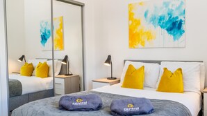 Ett hotellrum med en säng, två sängbord, en spegel och konstverk på väggarna.