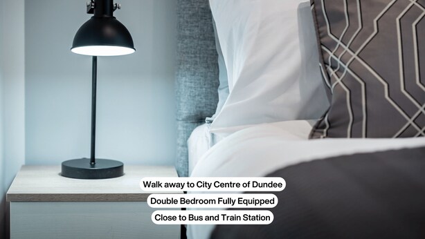A double bedroom with a modern lamp, a patterned pillow, and a view of a city center. - Trades Lane by Central Serviced Apartments - City Centre (Dundee)