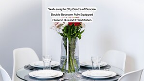 A double bedroom with a glass table set for dining, a vase with flowers, and a city center sign. - Trades Lane by Central Serviced Apartments - City Centre (Dundee)