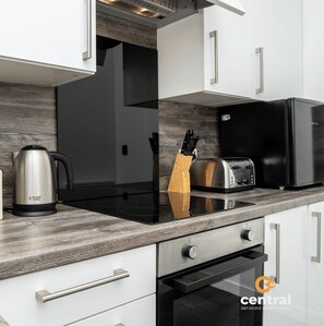 Eine moderne Küche mit weißen Schränken, einer Holzrückwand, einer schwarzen Induktionskochplatte, einem Toaster und einer Kaffeemaschine.