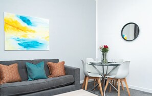 Ein modernes Wohnzimmer mit grauem Sofa, Couchtisch und Essbereich mit Glastisch und Stühlen.