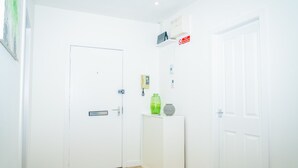 A clean, white room with a door, a small table with a green bottle, and a red no-smoking sign on the wall. - The Bond by Central Serviced Apartments - City Centre (Dundee)