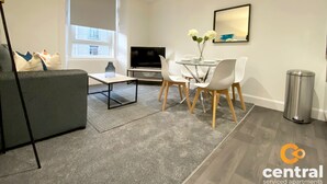 Ett modernt vardagsrum med en soffa, ett soffbord, en TV och en matplats med stolar och ett glasbord.