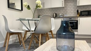 Ett modernt kök med vita skåp, ett matbord med glasskiva och en vas med blommor.