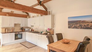 A kitchen with white cabinets, a wooden dining table with chairs, and a large painting on the wall. - 2 bedroom accommodation in Wrelton, near Pickering (Wrelton, near Pickering)
