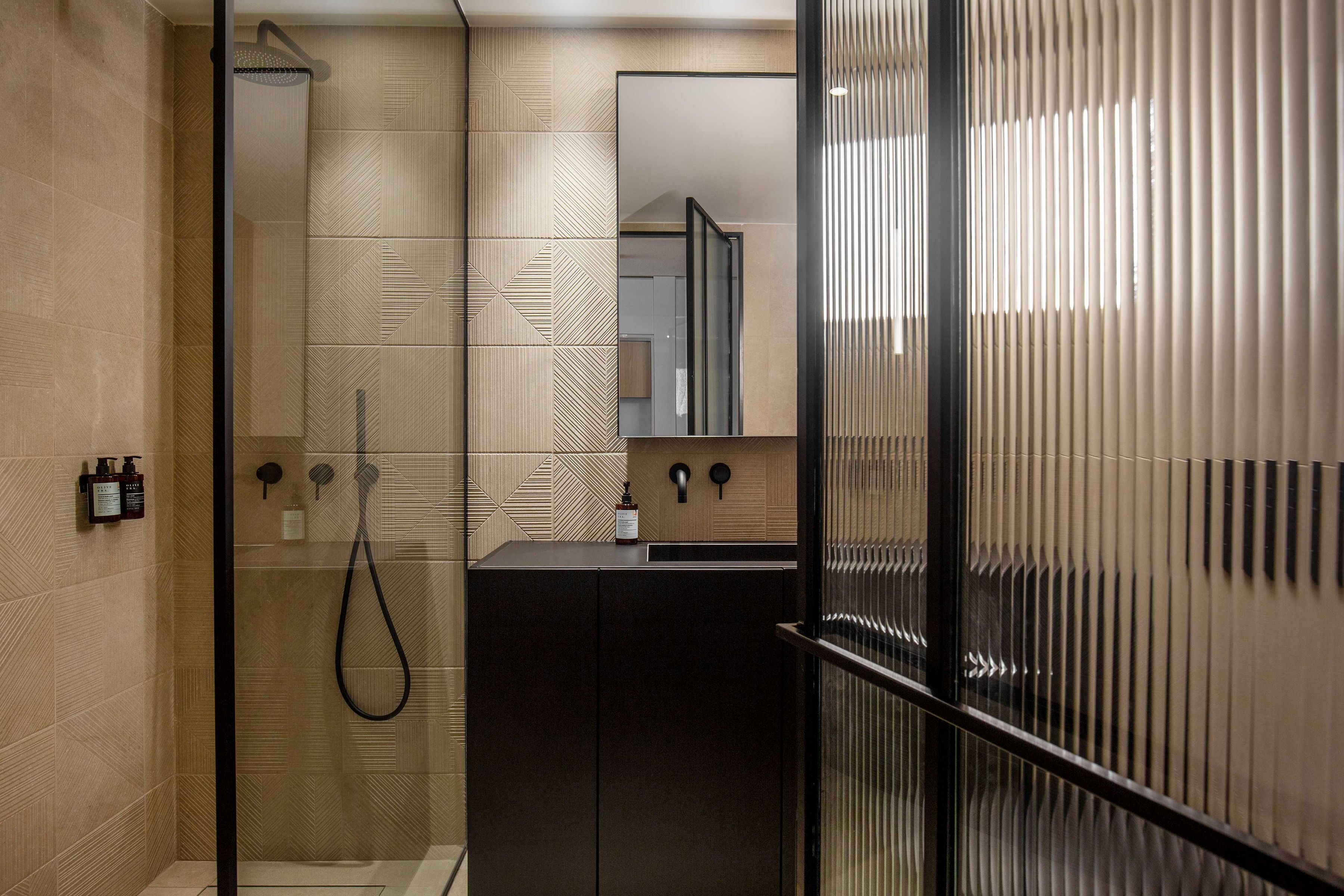Un baño moderno con ducha envuelta en vidrio, tocador oscuro y un espejo grande.