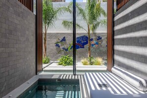 Un espace piscine intérieure moderne avec un mur en verre, une petite piscine et un banc.