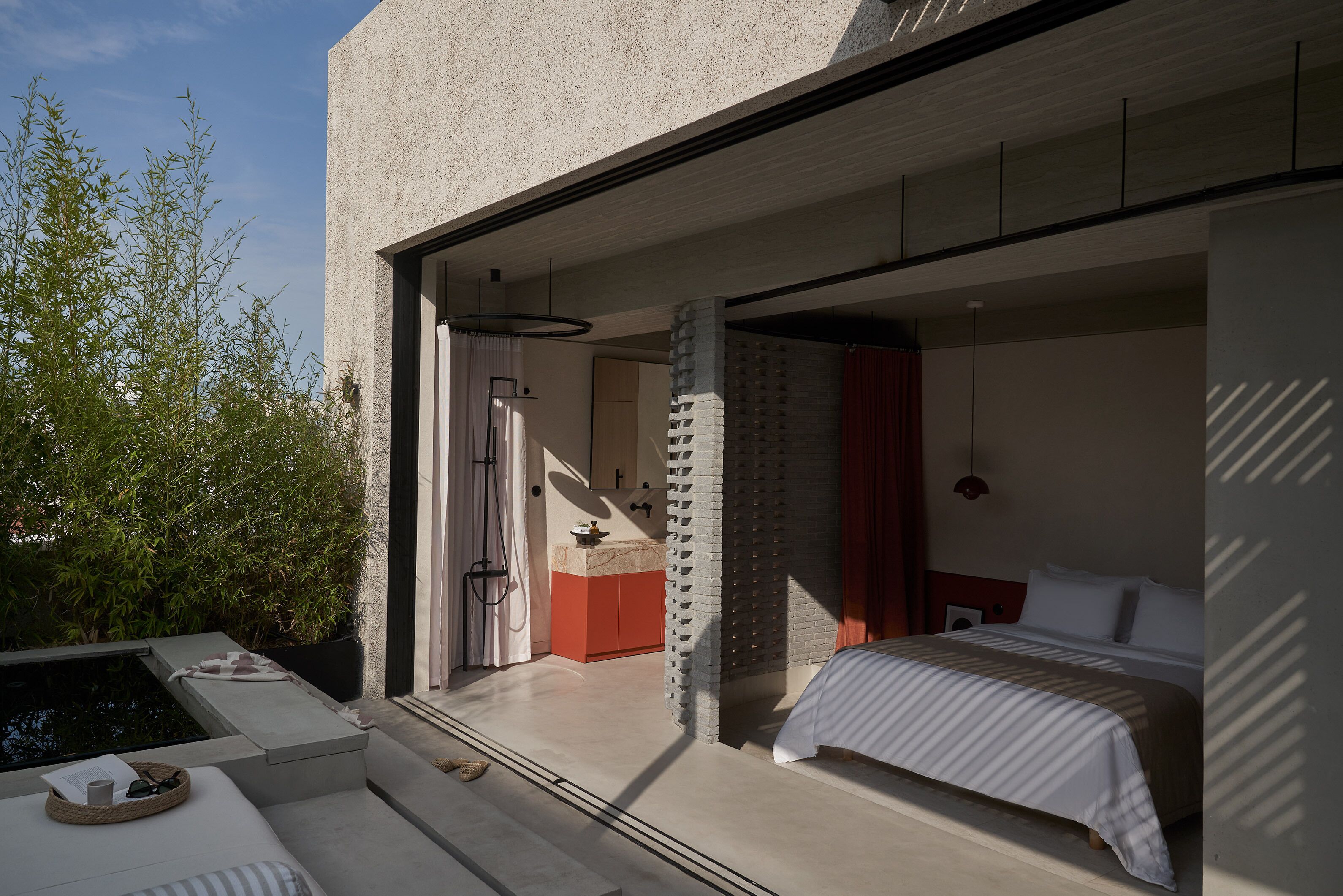A modern bedroom with a large bed, a small bathroom, and a view of the outdoors.