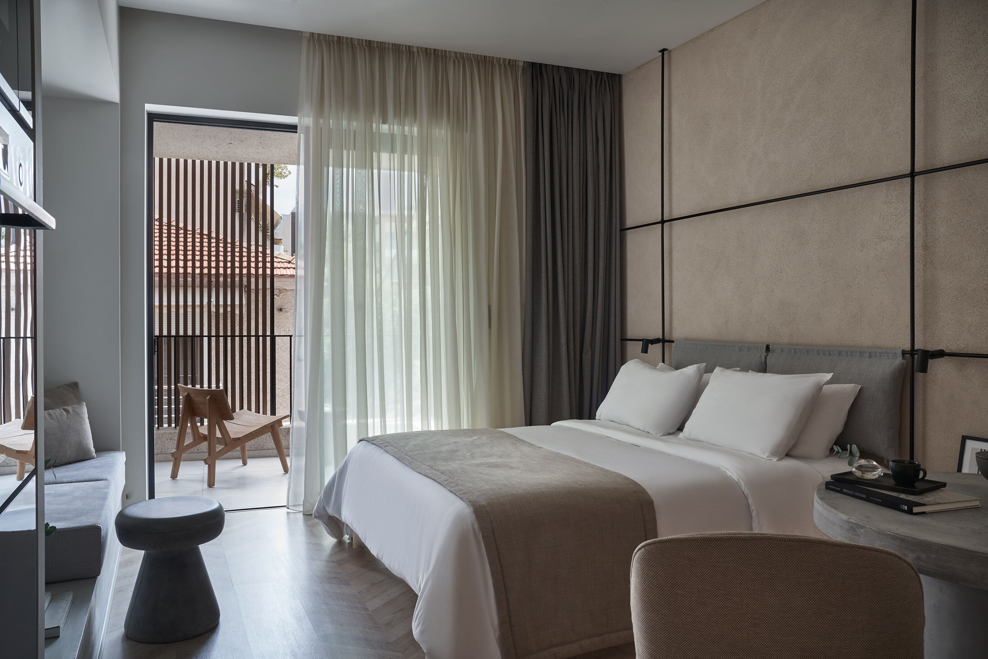 A modern hotel room with a large bed, a seating area with a chair and a small table, and a view of the outside balcony.