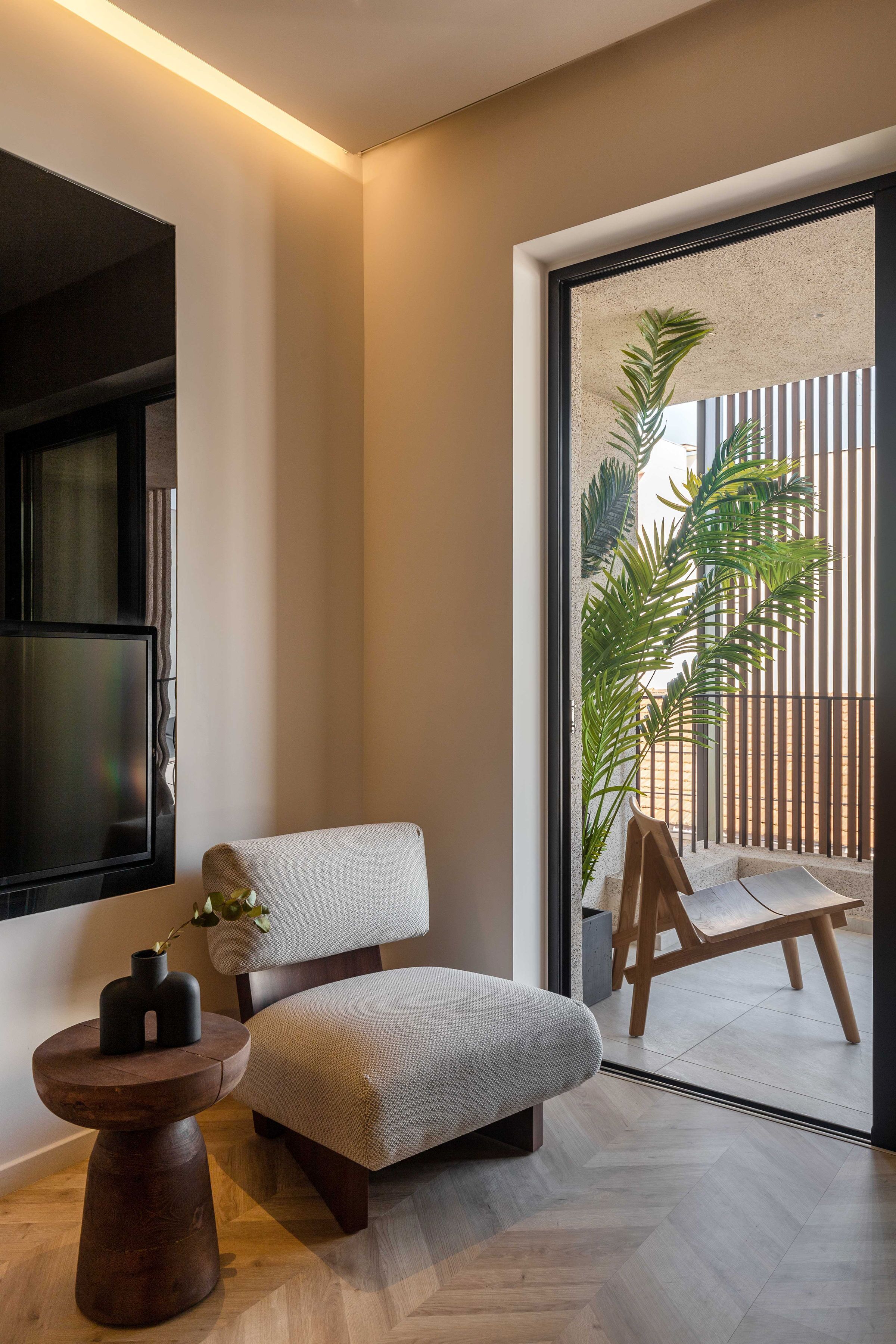Una sala moderna con un sofá, una mesita auxiliar, una planta en maceta y vistas al exterior a través de un ventanal.
