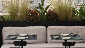 A rooftop seating area with two tables, each with a bowl, glass, and plate. - The Newel Psychiko (Athens)