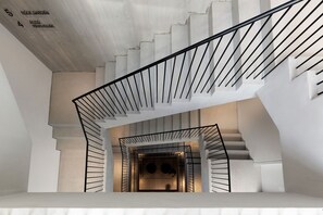 Un escalier moderne avec une rampe en métal noir et un plafond en béton où sont indiqués les numéros des chambres.