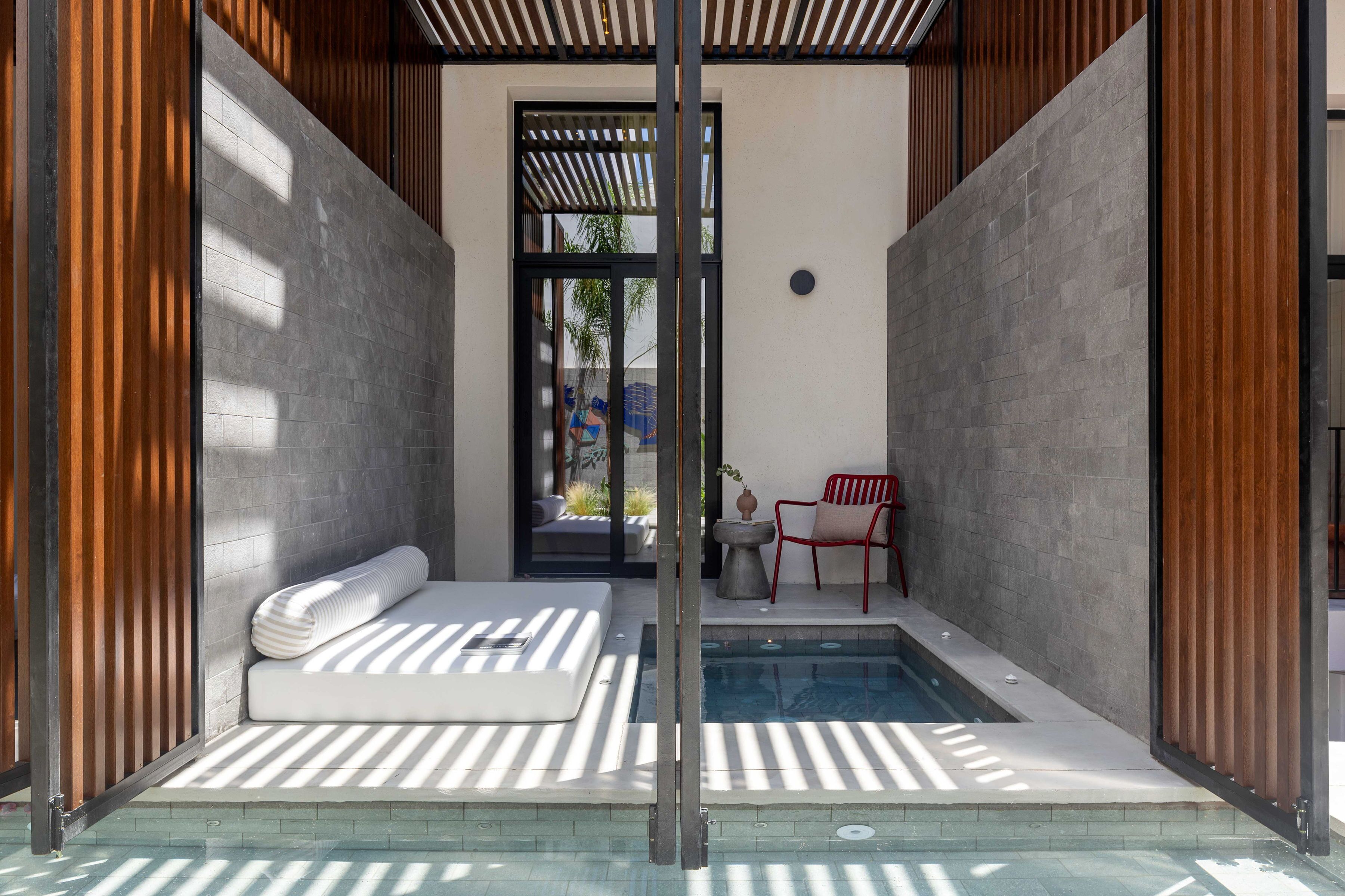 A modern spa area with a small pool, a massage table, and a red chair.