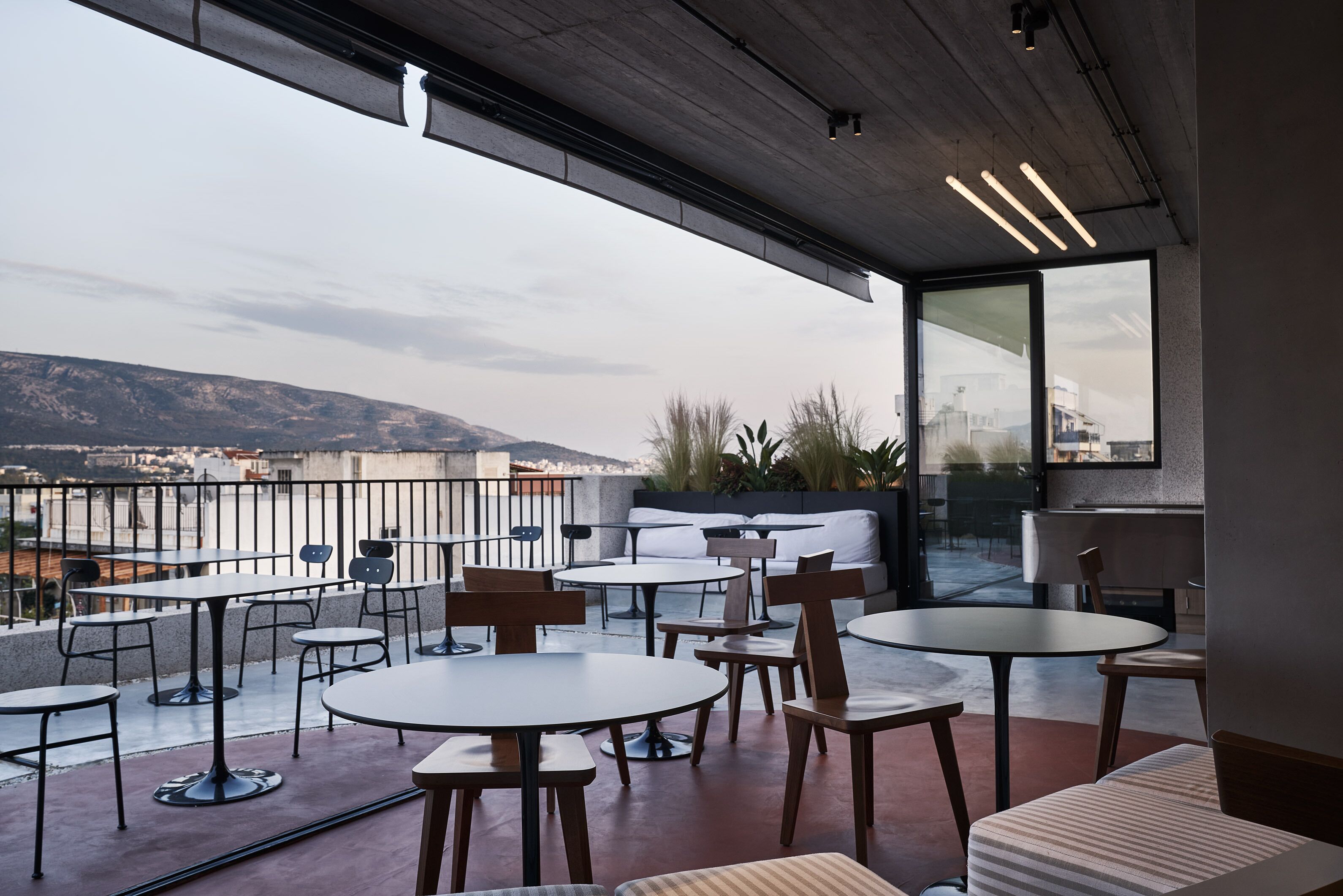 Terraza en la azotea con mesas y sillas, vistas panorámicas de la ciudad y un diseño arquitectónico moderno.