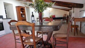 A dining area with a wooden table and chairs, a vase with flowers, and a wine bottle. - Le Grenier du Vissou (Cabrières)