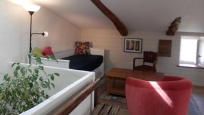 A cozy room with a bed, a wooden table, a red chair, a lamp, and a plant. - Le Grenier du Vissou (Cabrières)