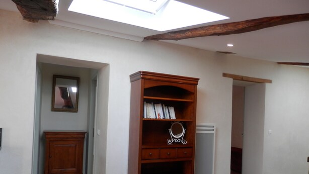 A room with a skylight, wooden bookshelves, a mirror, and a small cabinet. - Le Grenier du Vissou (Cabrières)