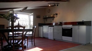 A kitchen with a dining table and chairs, white cabinets, a built-in oven, and a window with a view. - Le Grenier du Vissou (Cabrières)