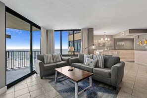 A modern living room with a sofa set, a coffee table, and a view of the beach through large windows.