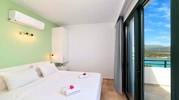 A bedroom with a bed, a nightstand, a wall-mounted air conditioner, and a view of a body of water through a sliding glass door.