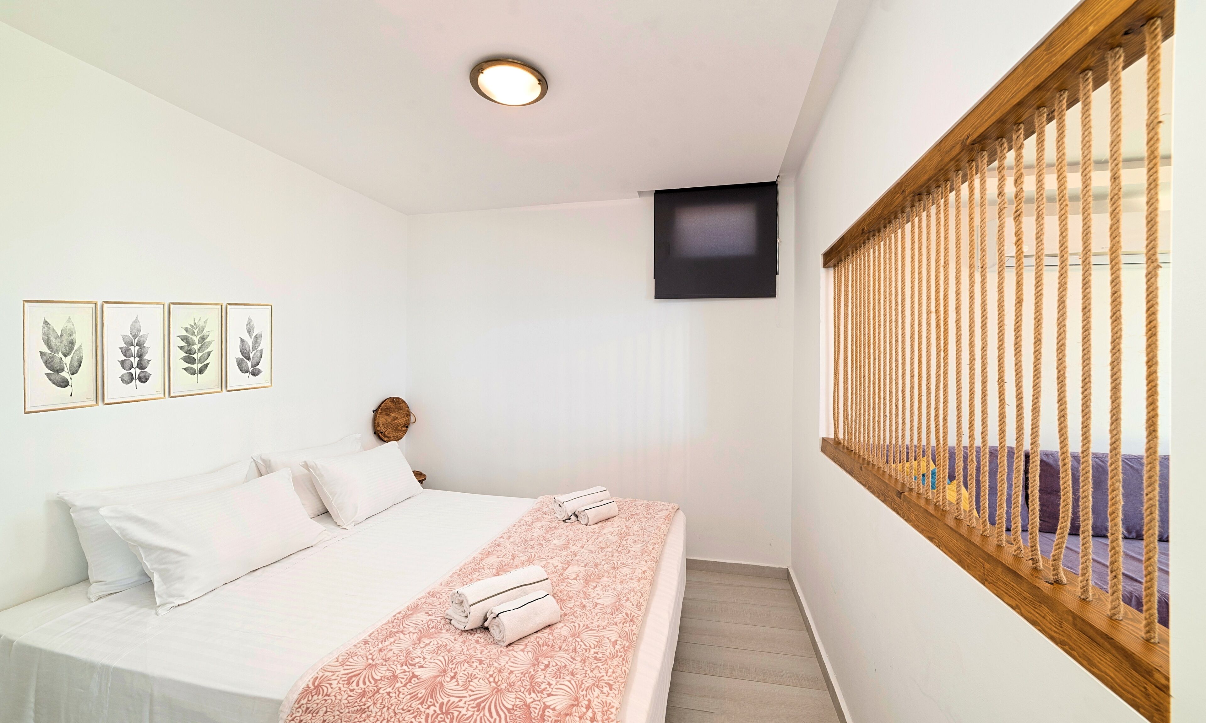 Ein Schlafzimmer mit Bett, einem an der Wand montierten Fernseher und einem Fenster mit Jalousie.
