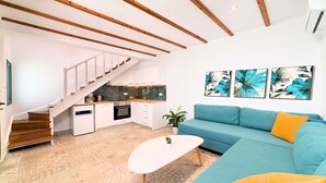 A modern living space with a kitchen, staircase, and a blue sofa. - Istron Homes (Agios Nikolaos)