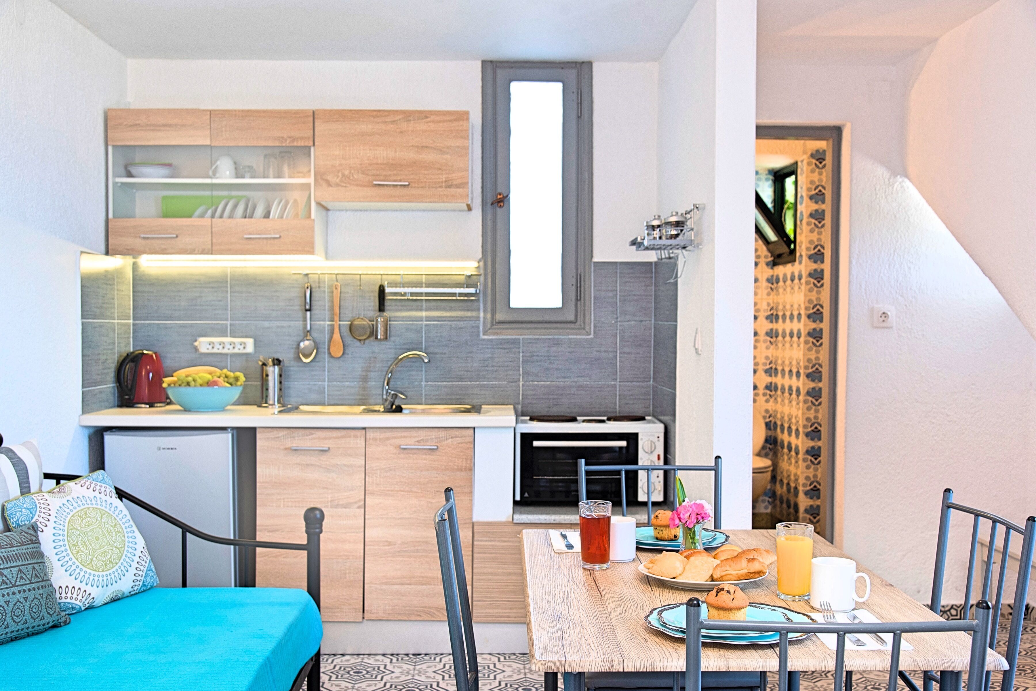 Una cocina compacta con armarios de madera, un microondas y un comedor con una mesa preparada para el desayuno.