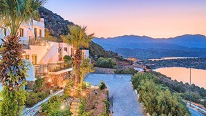 A coastal property with a paved pathway, white buildings, and a view of the sea and mountains. - Istron Homes (Agios Nikolaos)